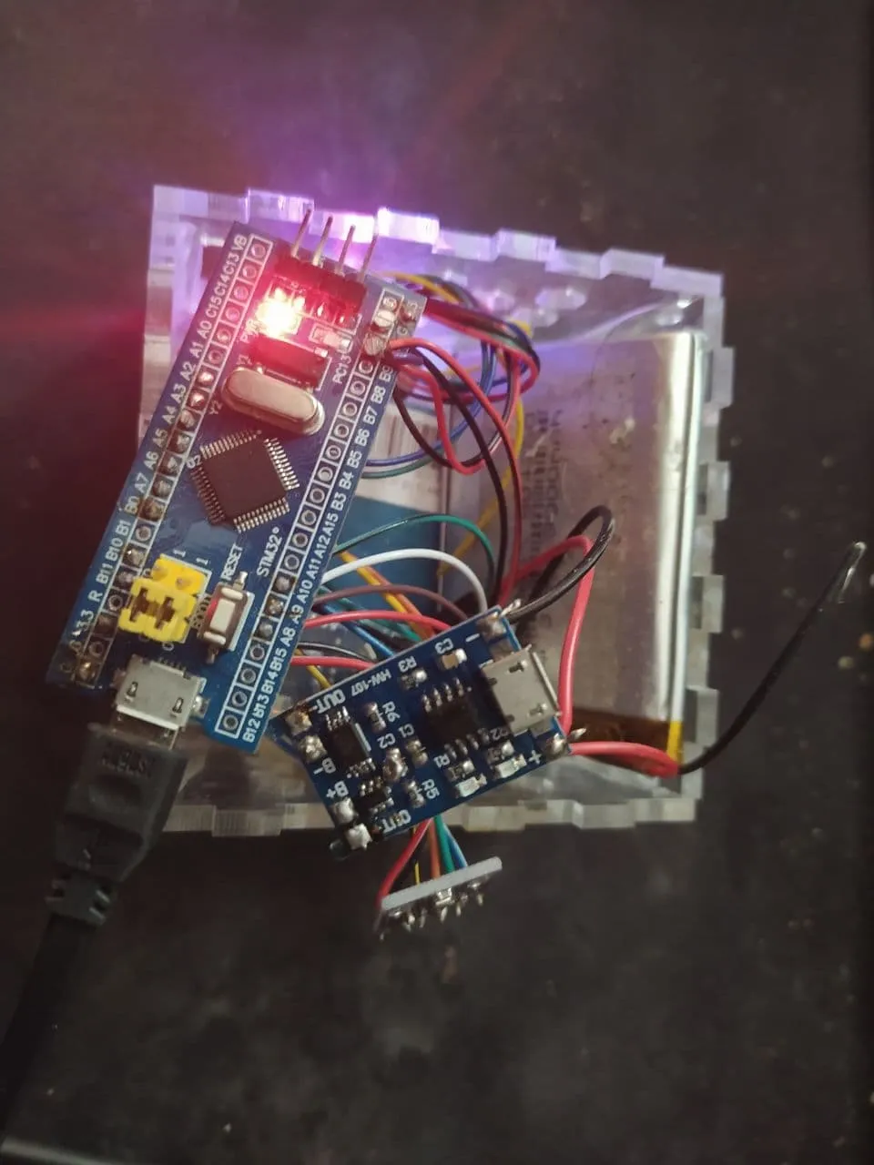 picture of an stm32 board connected to a variety of components. there is a laser cut acrylic storage box in the background, and the stm32 board has a lit LED