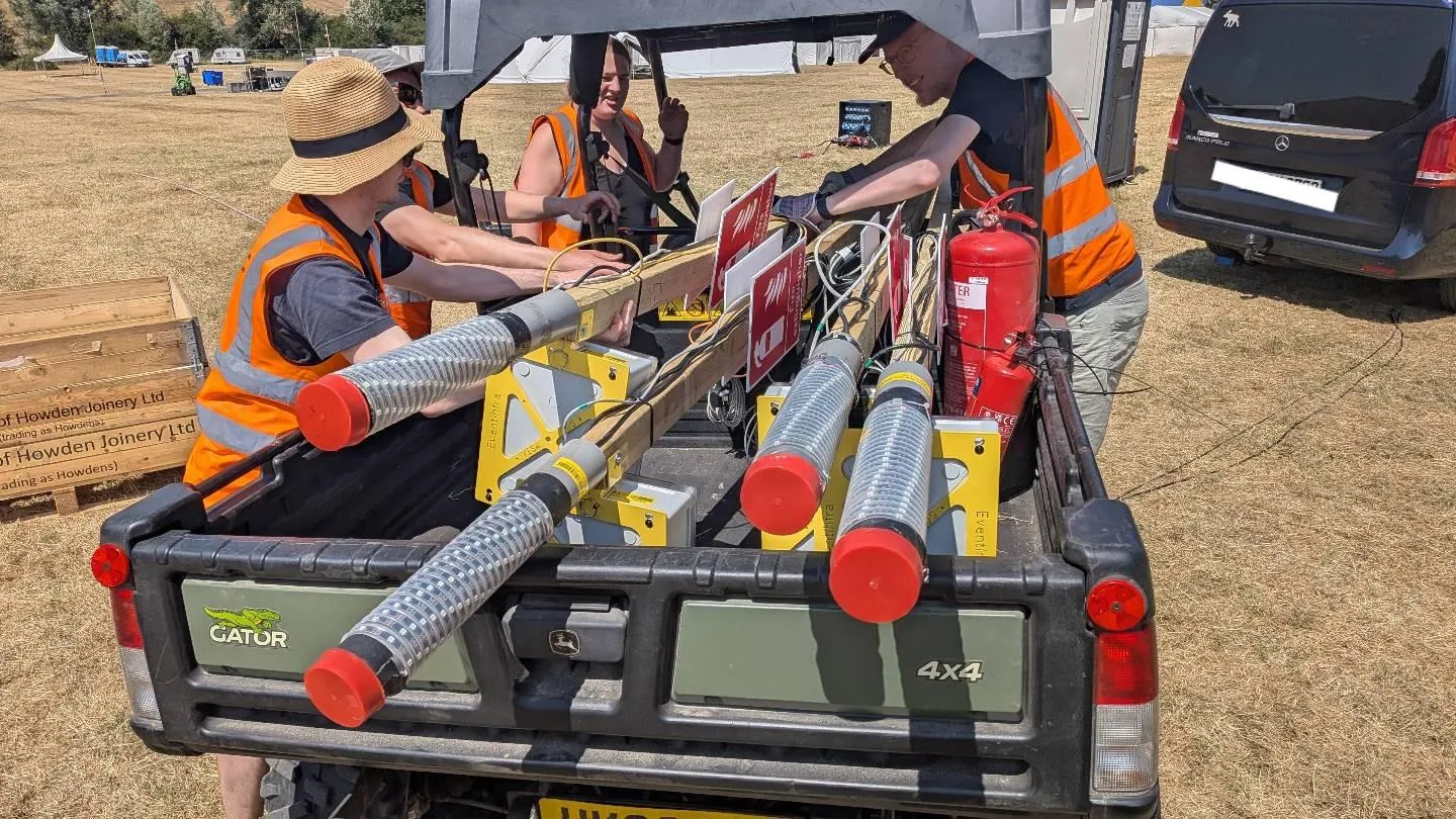 picture of a gator loaded with assembled datenklo poles. 4 people with hi-vis are visible, one sitting in the hatchback section, one behind them, myself in the center (having a bad hair and sun day) and another wrestling the poles to the passenger side of the vehicle.