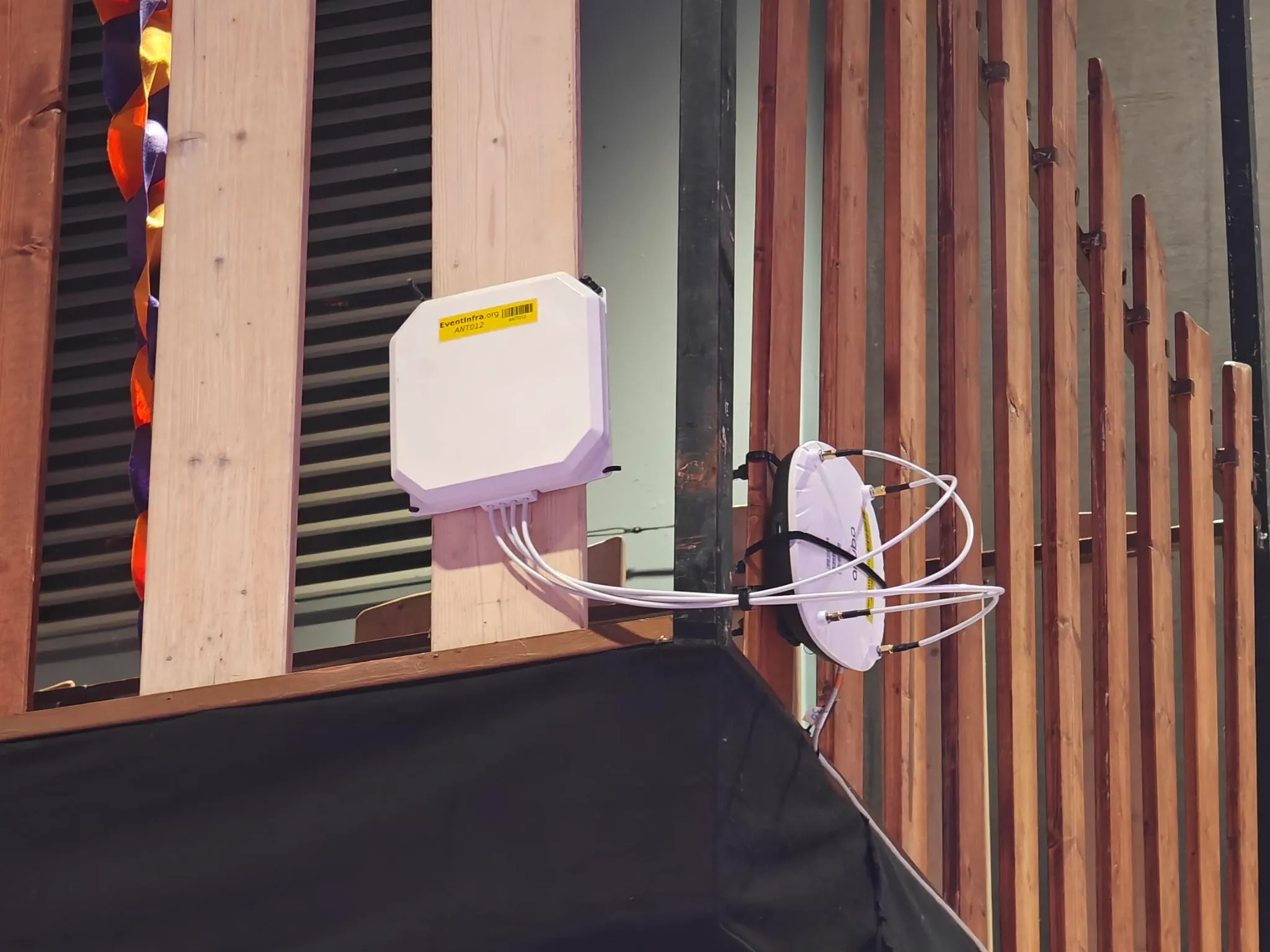 picture of a wooden railing, with an AP and a 6GHz extension antenna zip tied to the outside