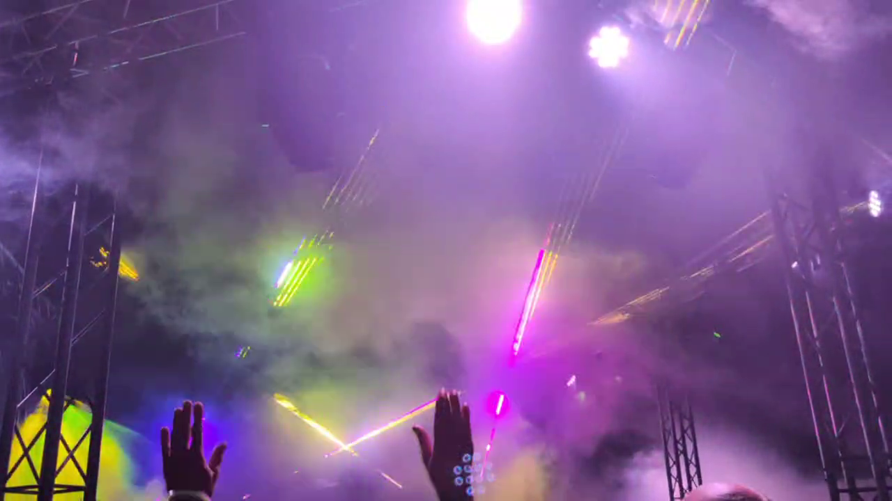 A music and light show, one can see a few "party hands" and lasers piercing through the atmospheric fog.