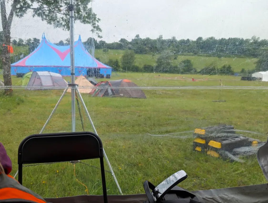 The view from the HQ tent. One can see a few tents next to a tree, an antenna of questionable origin, and one of the event stages in the background